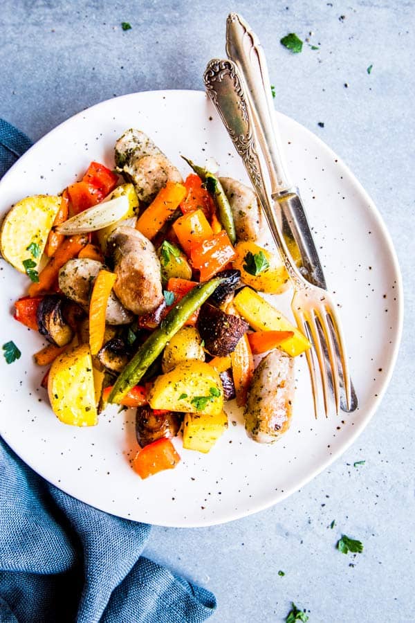 sausage potato and vegetables sheet pan dinner on a white plate with a fork and knife