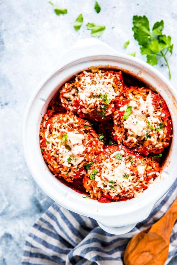 slow cooker stuffed peppers in a white crock with a wooden spoon