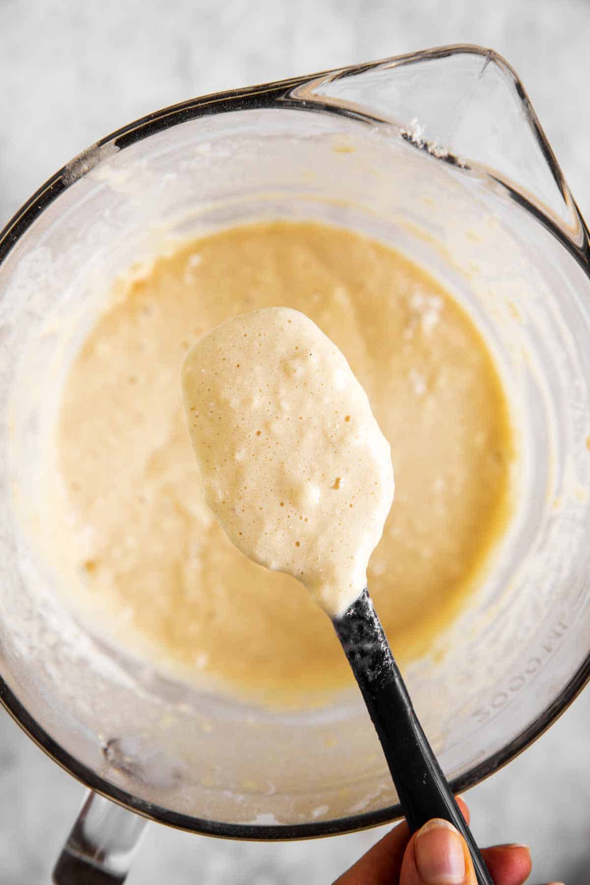 female hand holding spatula with pancake batter over glass bowl