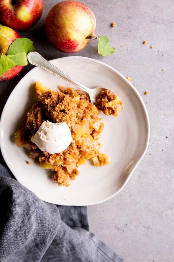 apple cobbler on a plate with ice cream, surrounded by fresh apples