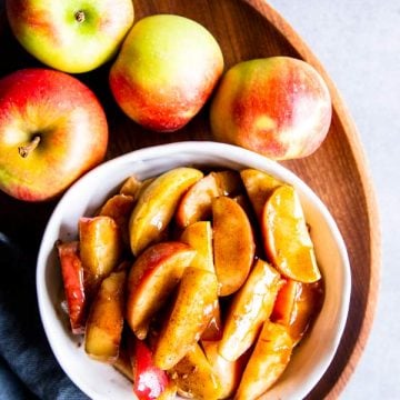 cinnamon apples in a white bowl with fresh apples around