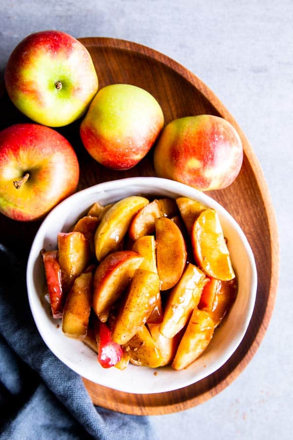 cinnamon apples in a white bowl with fresh apples around