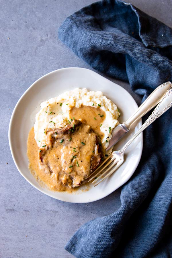 pork chops and mashed potatoes with sour cream sauce on a white plate