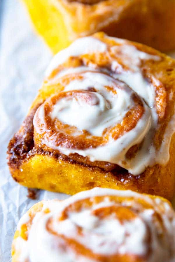 close up photo of a frosted pumpkin cinnamon roll