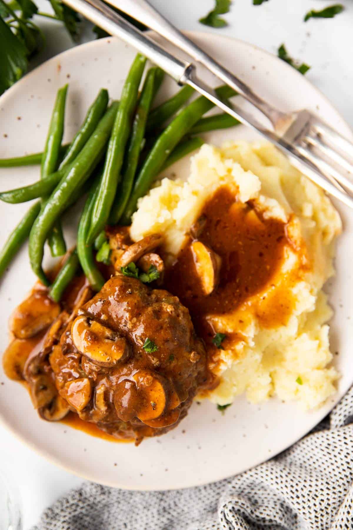 white plate with Salisbury steak, mashed potatoes and green beans