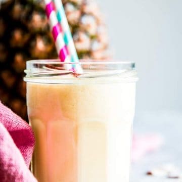 pina colada smoothie in a glass with straws and a fresh pineapple