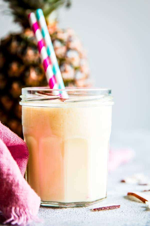 pina colada smoothie in a glass with straws and a fresh pineapple