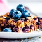 slice of blueberry baked oatmeal on a plate with fresh blueberries