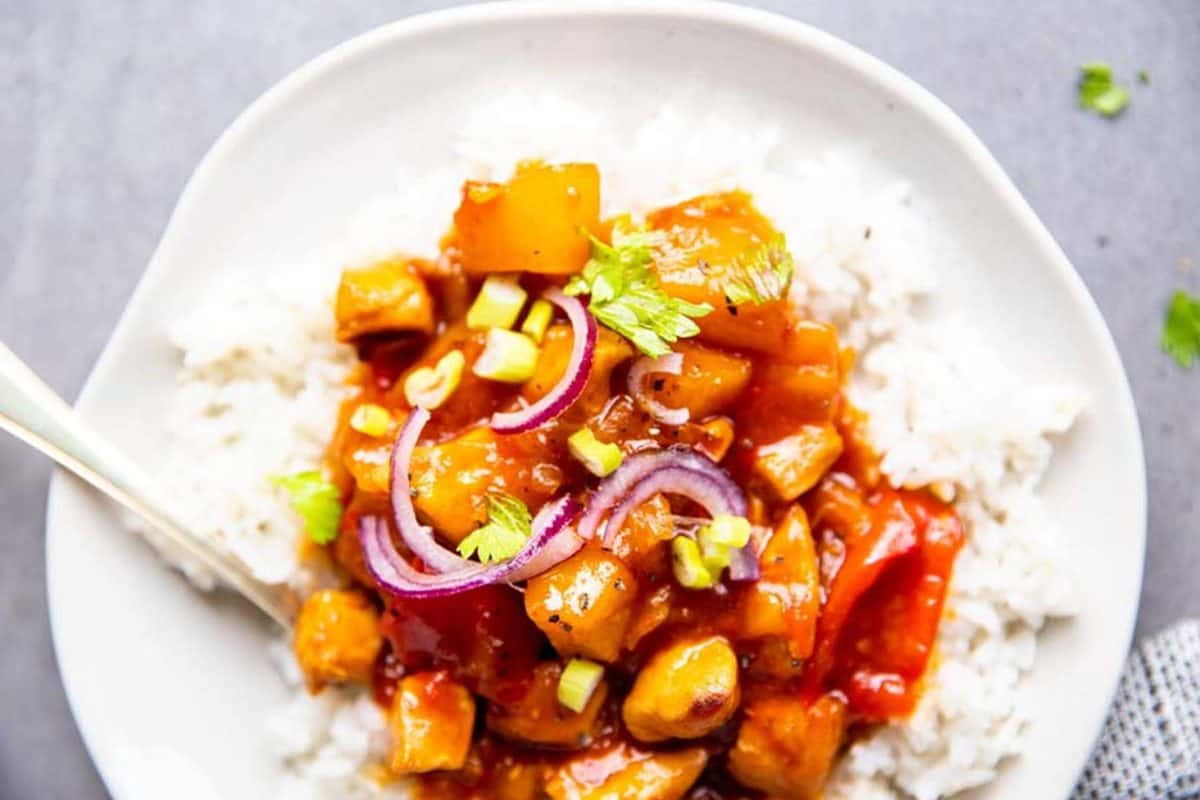 close up photo of a white plate with rice and pineapple chicken