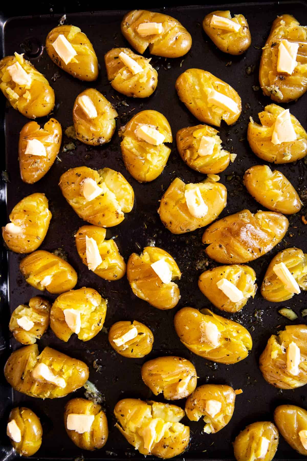 smashed potatoes dotted with butter on black pan