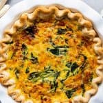 white pie dish with a spinach bacon quiche inside