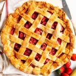 overhead view of strawberry rhubarb pie with dish towel and fresh fruit next to it