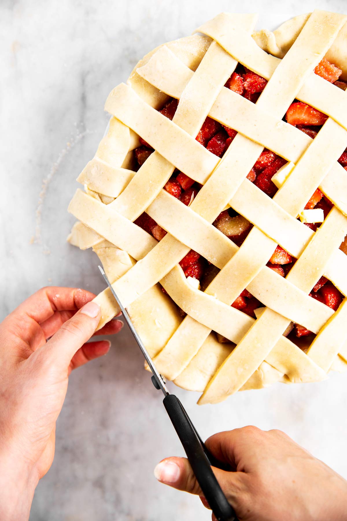 female hands using kitchen shears to trim crust around unbaked pie