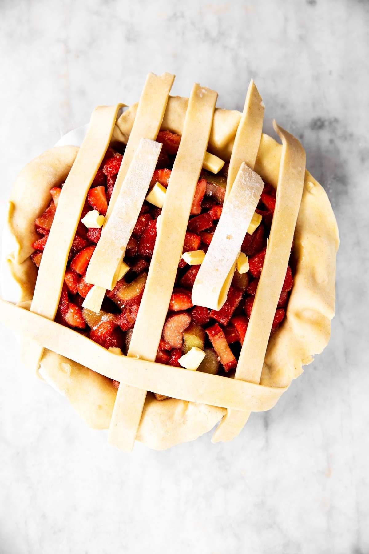 first step of lattice crust weave on top of strawberry rhubarb pie