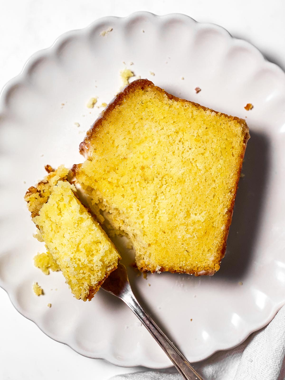 slice of lemon loaf cake on white plate with a fork taking a bite out