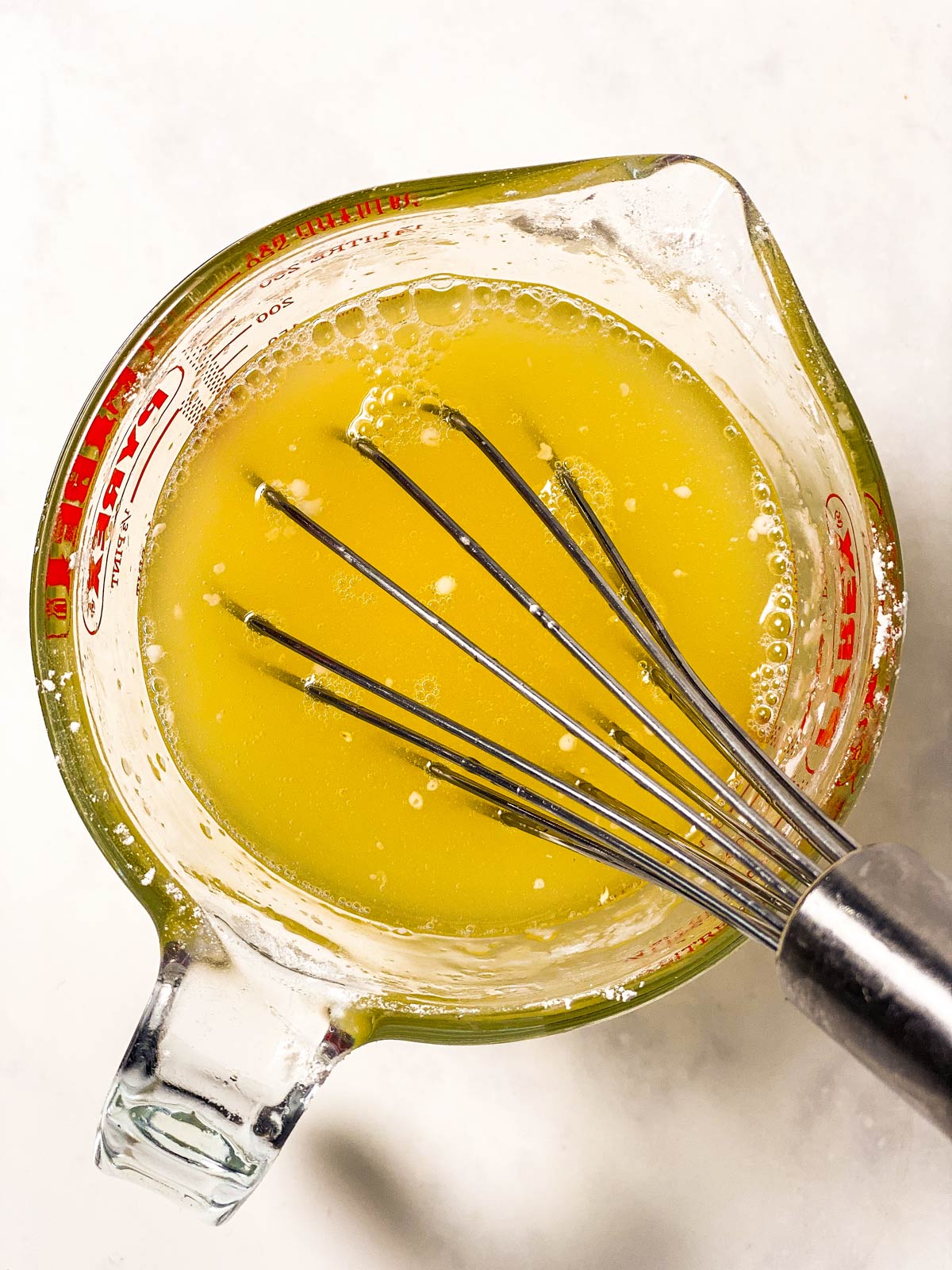 lemon drizzle syrup in small glass measuring jug with whisk