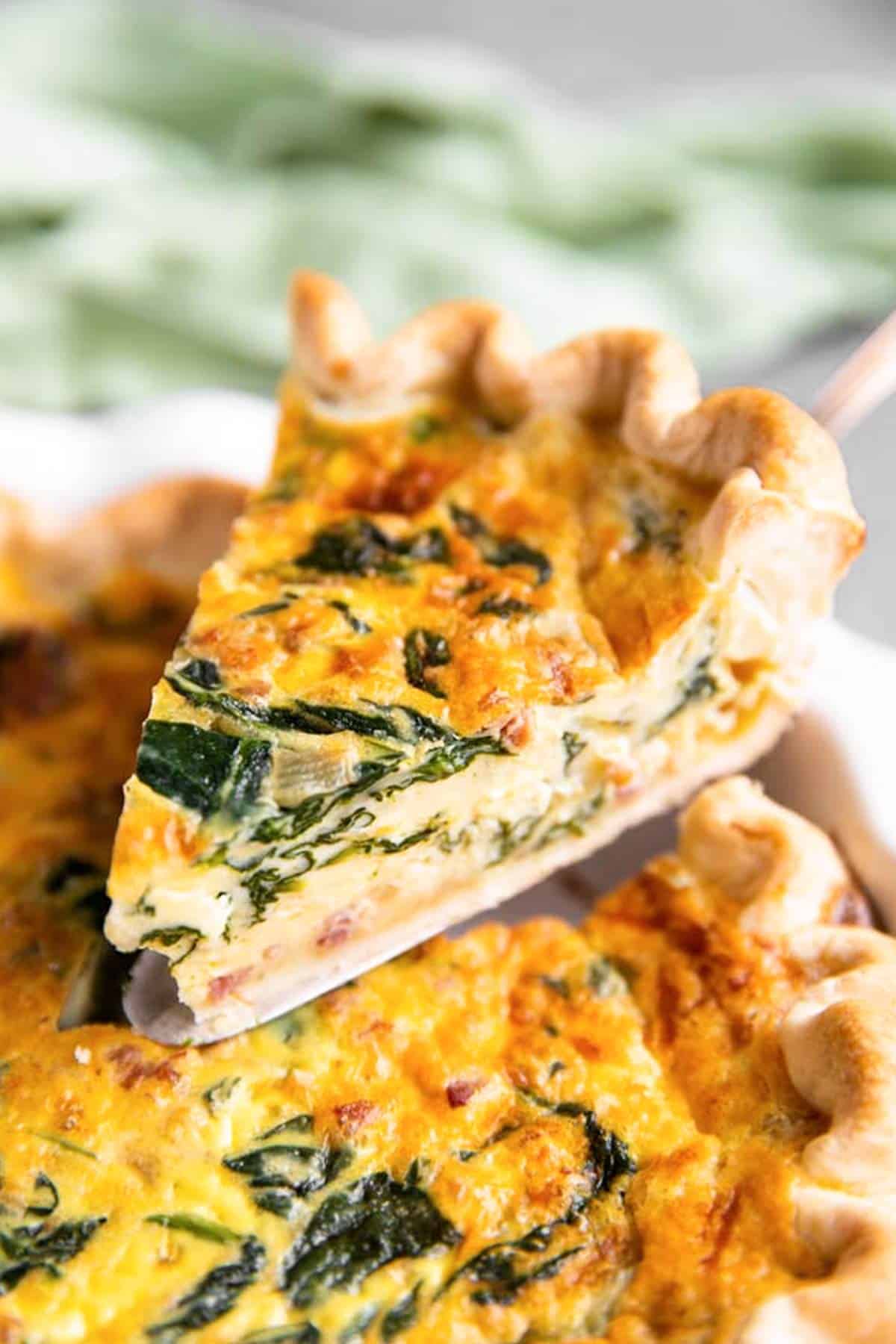 lifting a slice of spinach bacon quiche from the pie dish