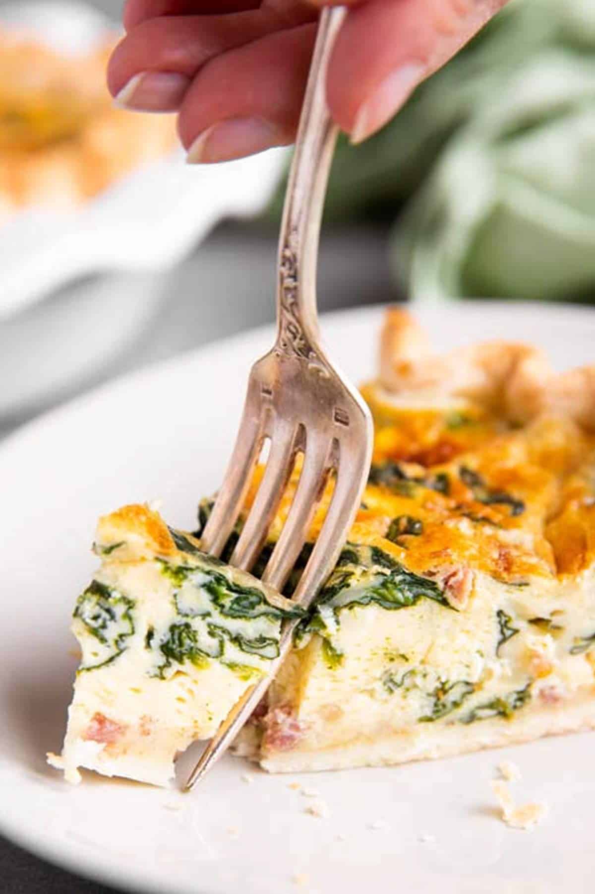 fork stuck in slice of spinach bacon quiche