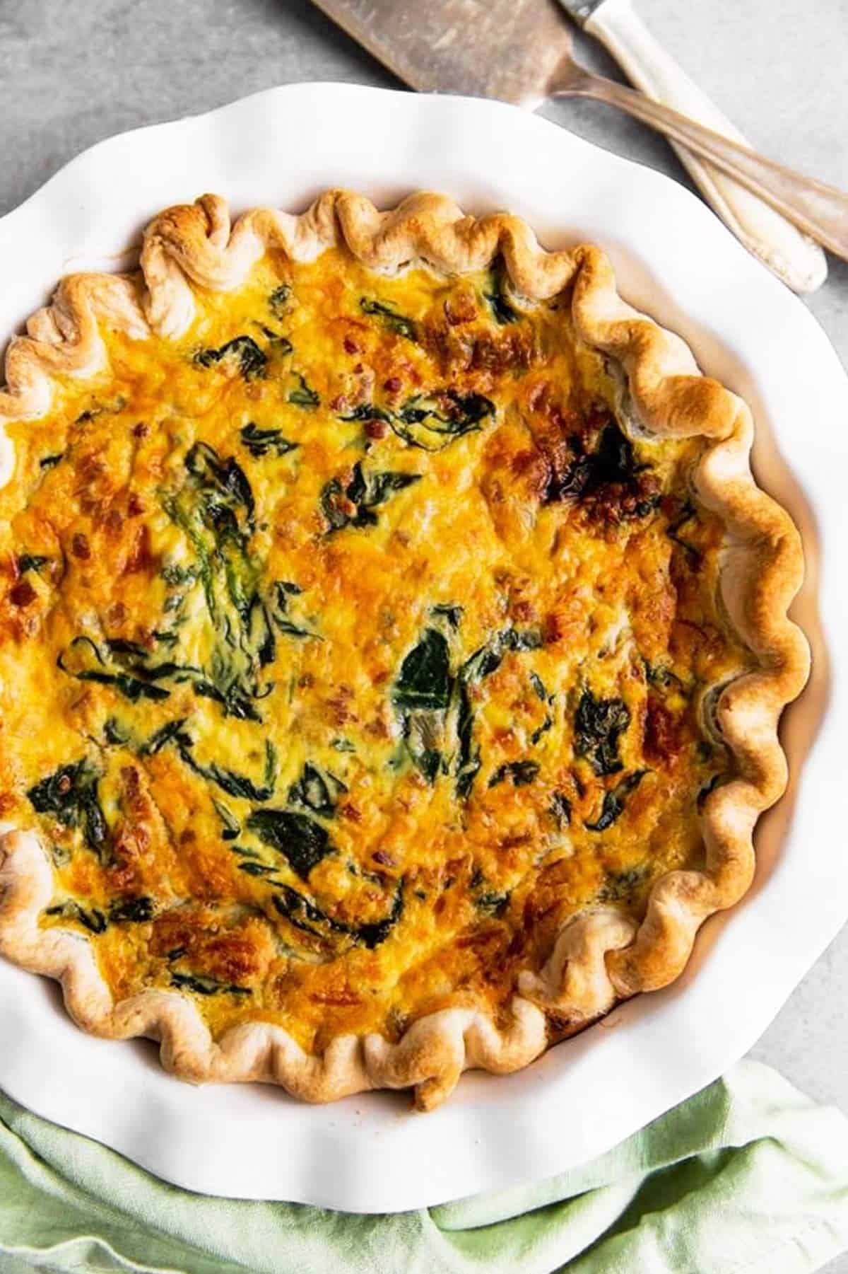 overhead view of baked spinach bacon quiche in white pie plate