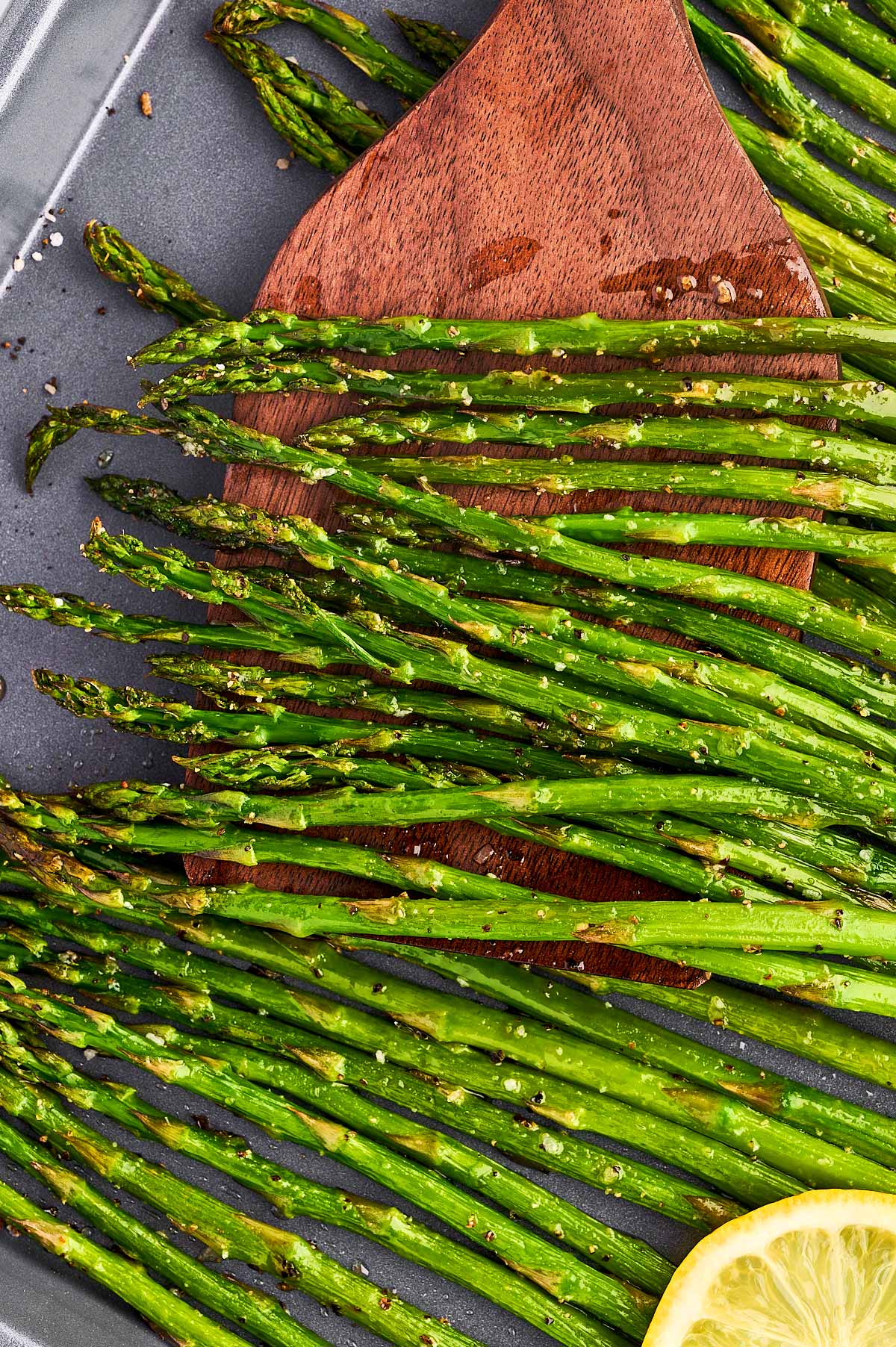 Scooping roasted asparagus with a wooden spatula.