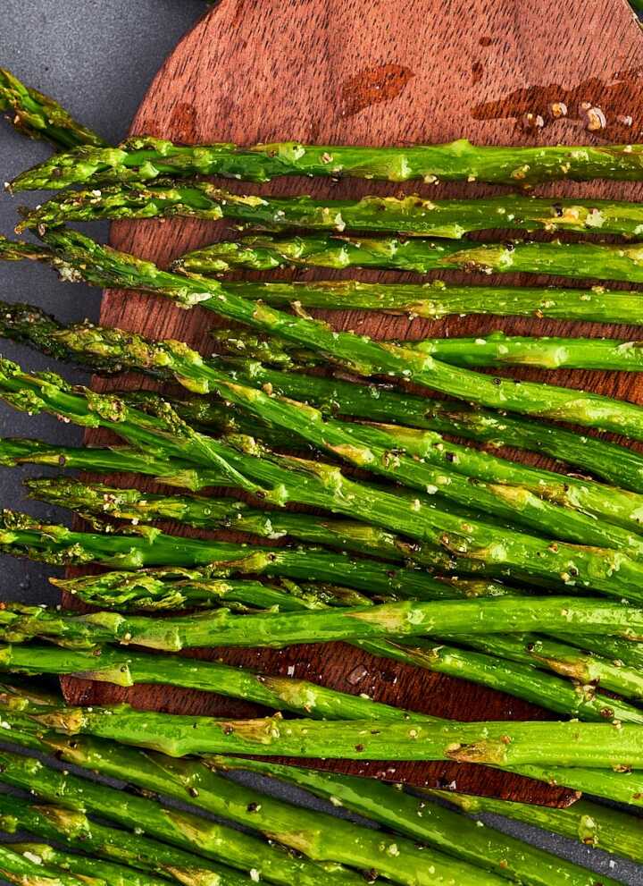 Scooping roasted asparagus with a wooden spatula.