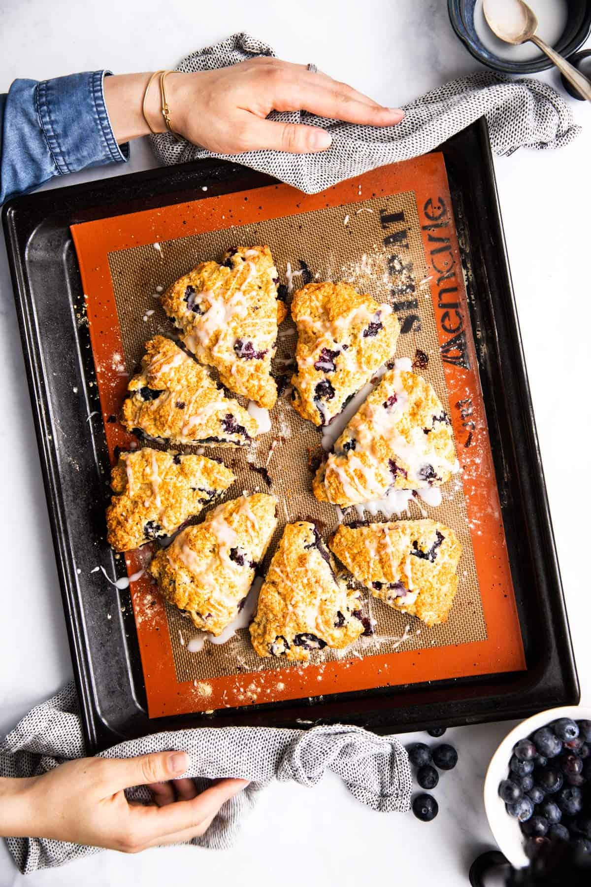 top down view on female hands holding baking sheet with blueberry scones