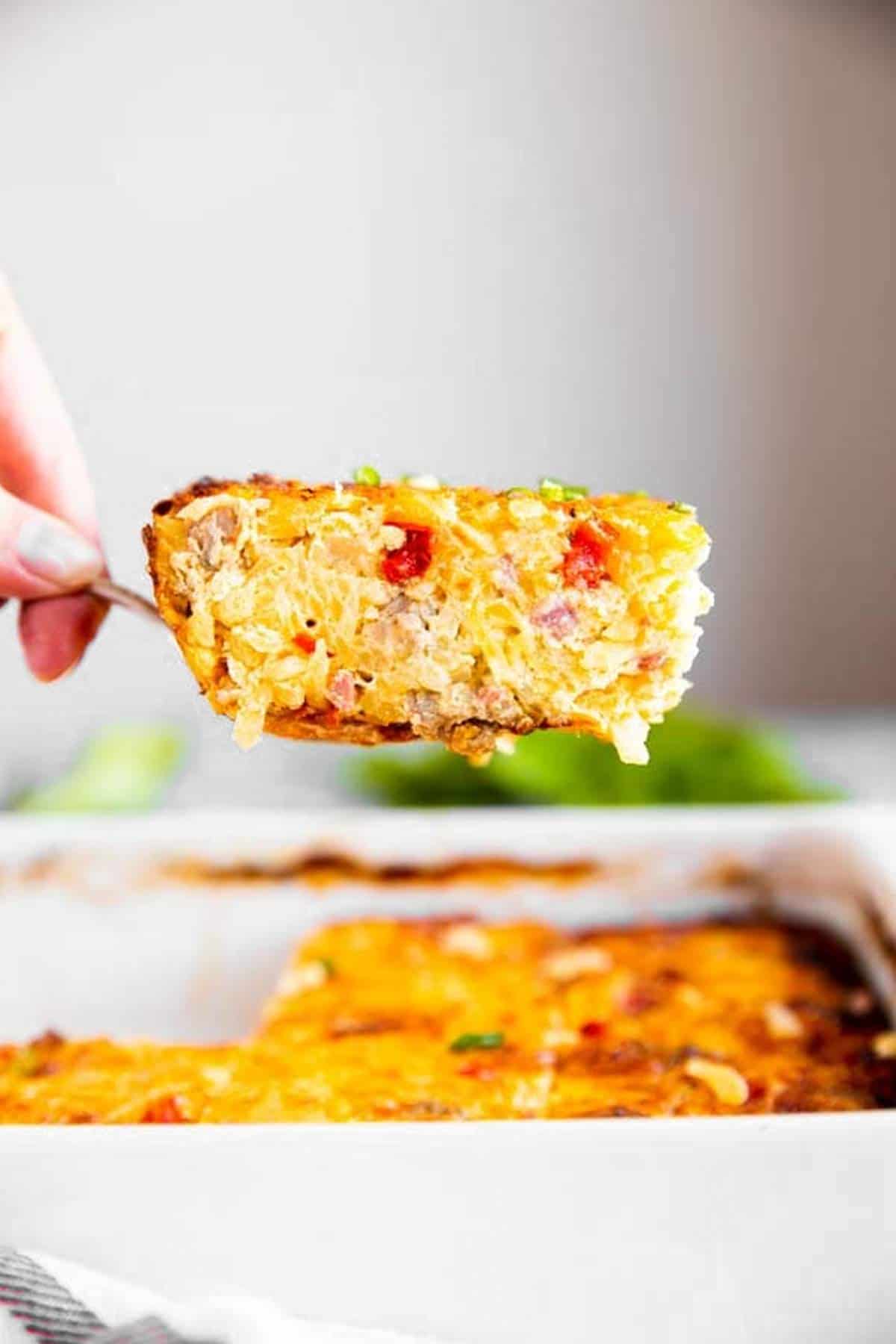 female hand lifting slice of hash brown breakfast casserole out of casserole dish