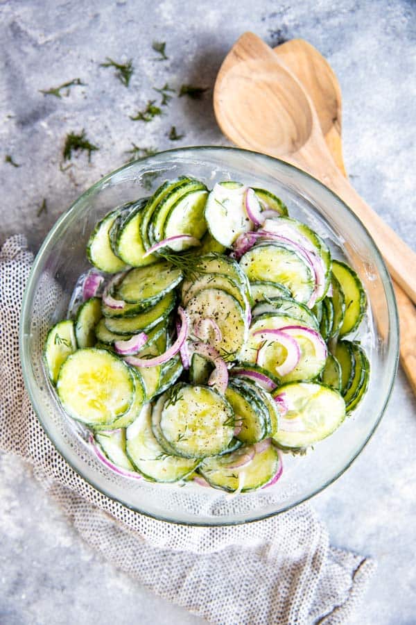 glass bowl with creamy cucumber salad and wooden salad tongues
