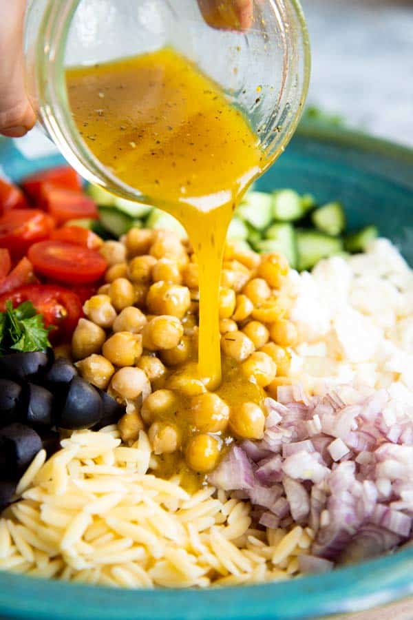 pouring dressing over greek orzo salad
