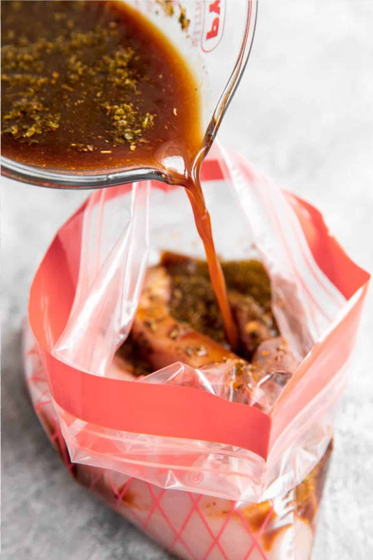 pouring balsamic marinade over raw chicken breast in a ziptop bag