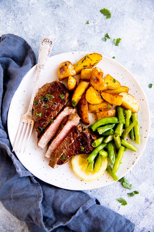 cooked steak on a white plate with potatoes and green beans