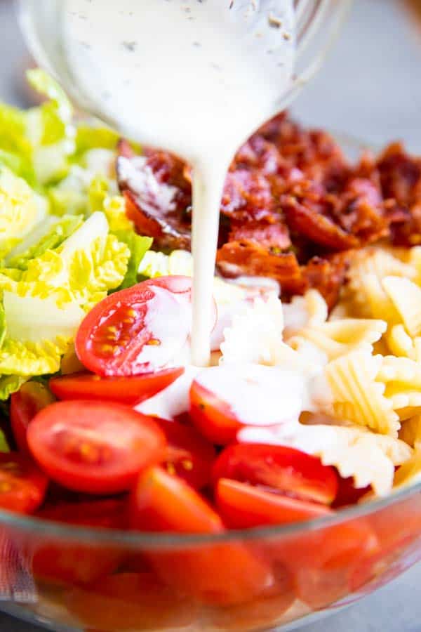 pouring ranch dressing over pasta salad