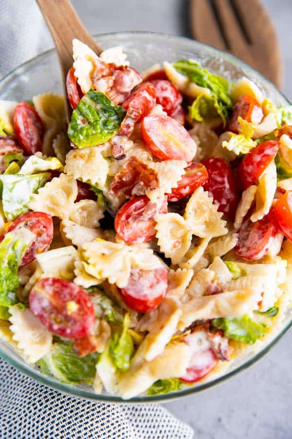 blt pasta salad in a glass bowl with wooden salad tongues