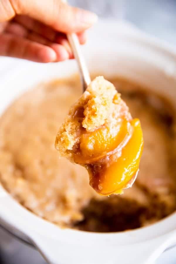 scooping peach cobbler from a slow cooker with a spoon