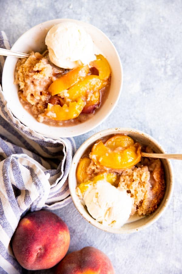 two white bowls with peach cobbler and vanilla ice cream