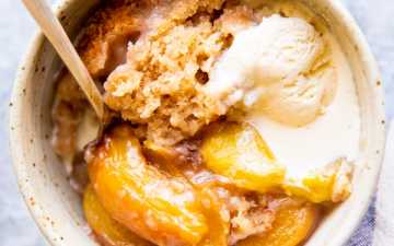 white bowl with peach cobbler, ice cream and a spoon, next to a striped tea towel