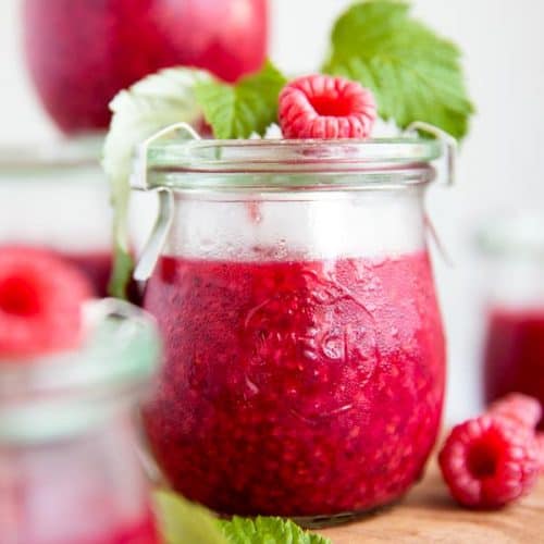 small glass jar with homemade raspberry jam, fresh raspberries and raspberry leaves