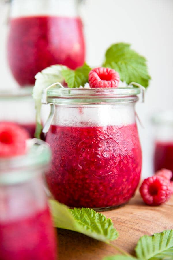 small glass jar with homemade raspberry jam, fresh raspberries and raspberry leaves