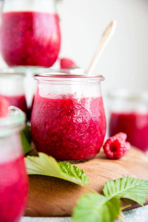 jar of raspberry jam with a spoon in it, next to more jam jars