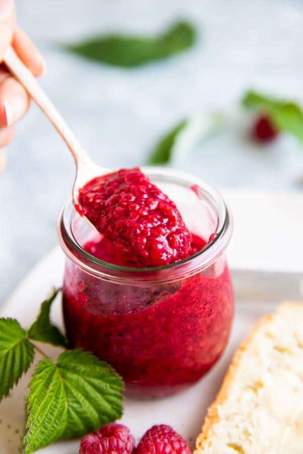 scooping freezer raspberry jam from a jam jar with a teaspoon