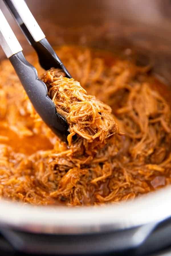 scooping pulled pork out of an instant pot with kitchen tongues