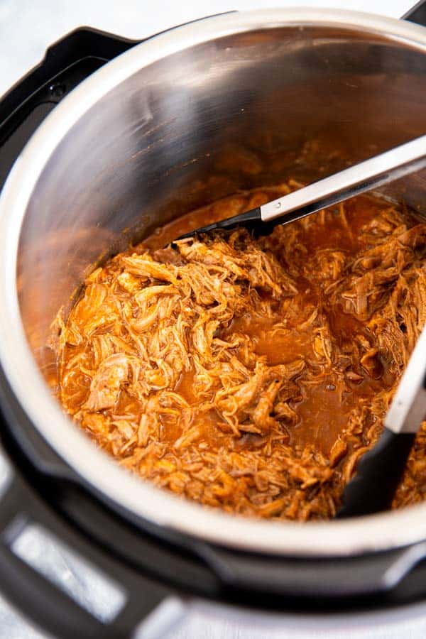 instant pot with honey bbq pulled pork inside, with kitchen tongues