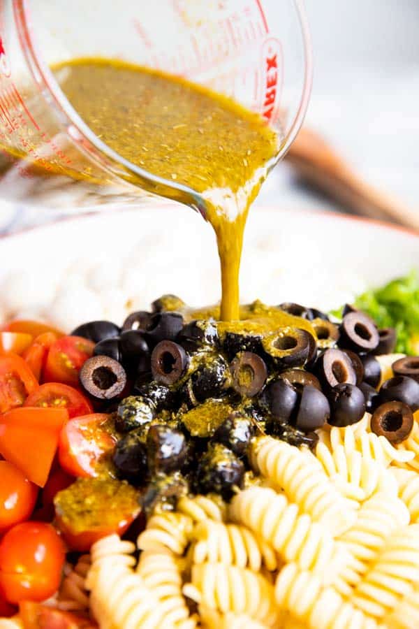 pouring pesto dressing over caprese pasta salad