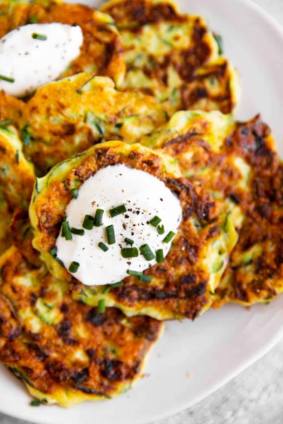 close up photo of zucchini fritters on plate with sour cream