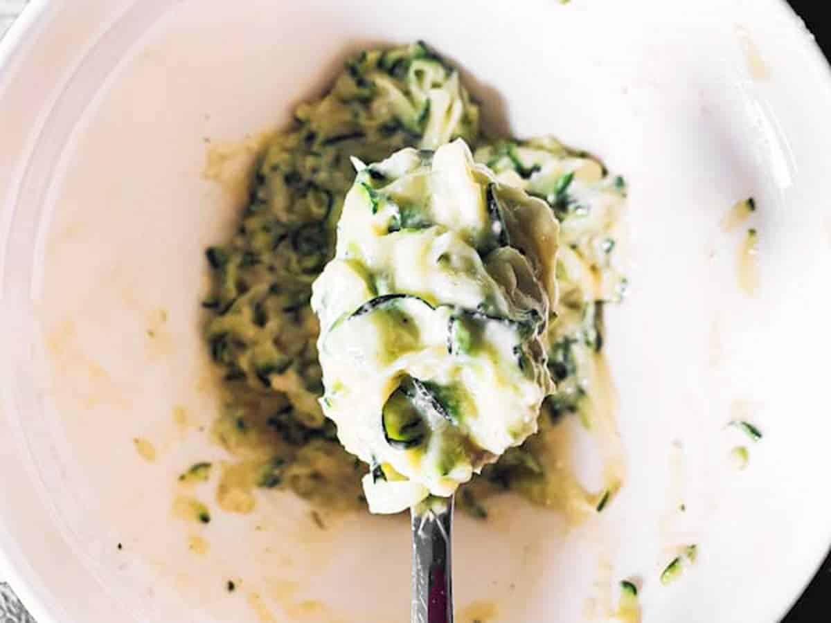 spoon scooping mixture for zucchini fritters from bowl