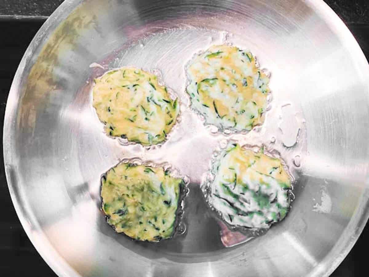 four zucchini fritters cooking in skillet
