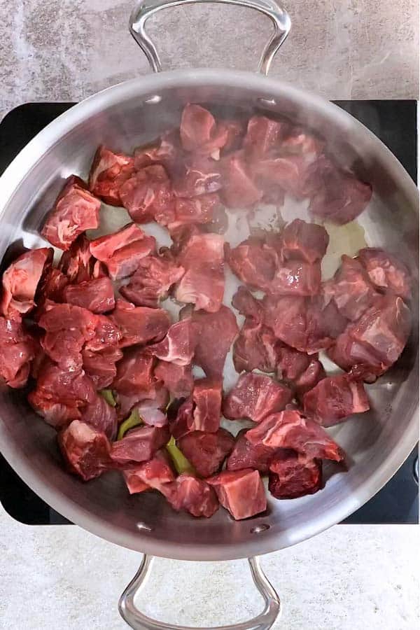 raw beef stewing meat in a skillet