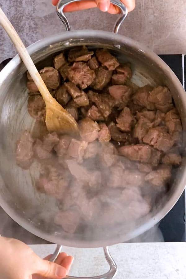 browned beef cubes in a skillet with a wooden spoon