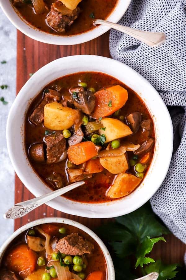 three white bowls with beef stew on a wooden board