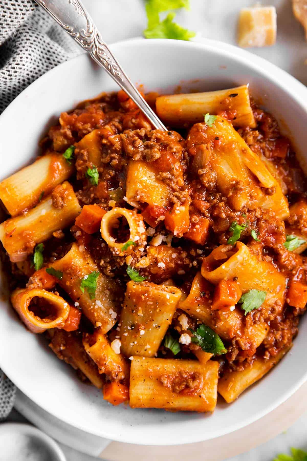 close up photo of rigatoni bolognese in white bowl with fork